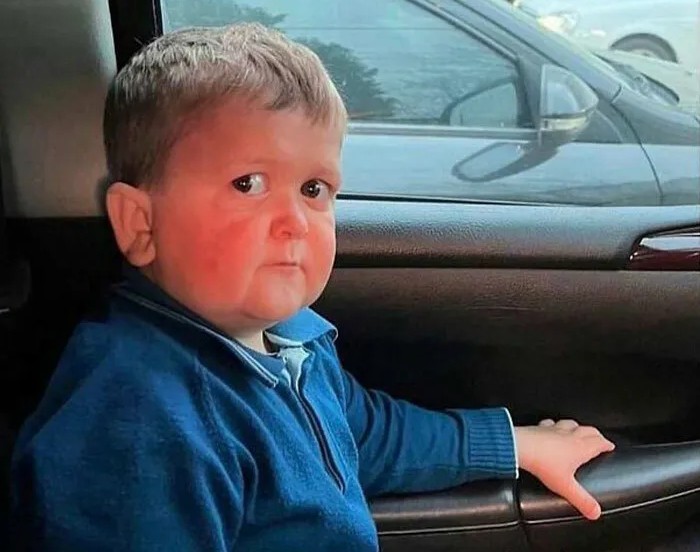 Dieťa v modrom svetri sedí v aute, pozerá sa von oknom a má vážny výraz.