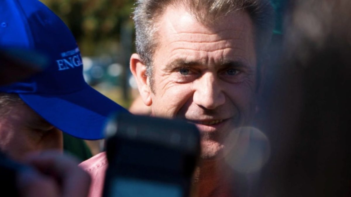 Osoba na open-air podujatí obklopená ľuďmi a fotografmi s modrou čiapkou v pozadí.