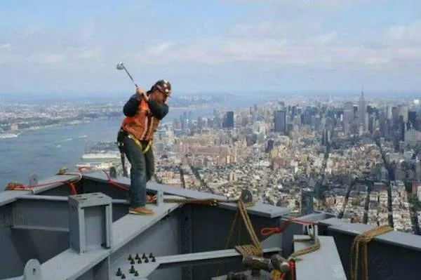 Robotník s golfovou palicou na streche mrakodrapu s výhľadom na mesto.