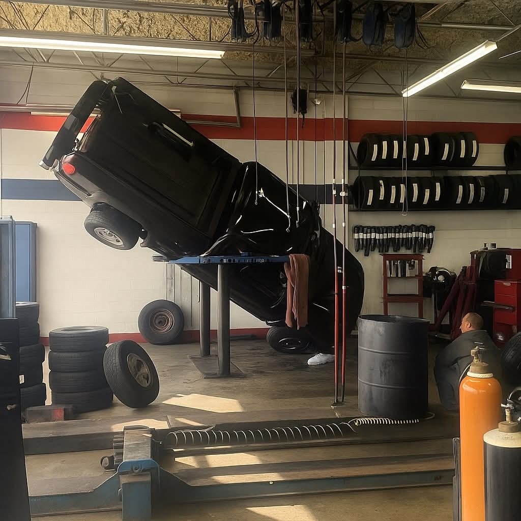 Auto prevrátené na boku v autoservise, technici analyzujú situáciu medzi pneumatikami a náradím.