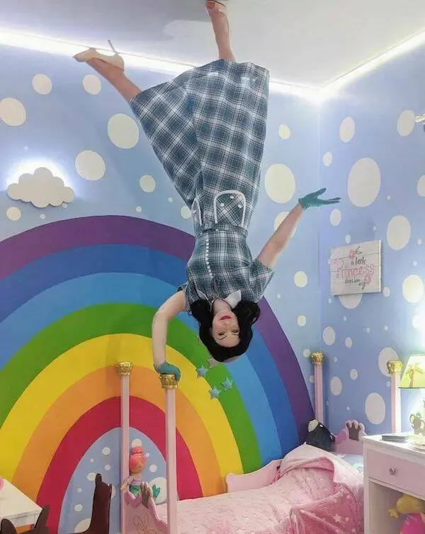 Osoba visí dolu hlavou v izbe s farebnou dúhou a bodkami na stenách.