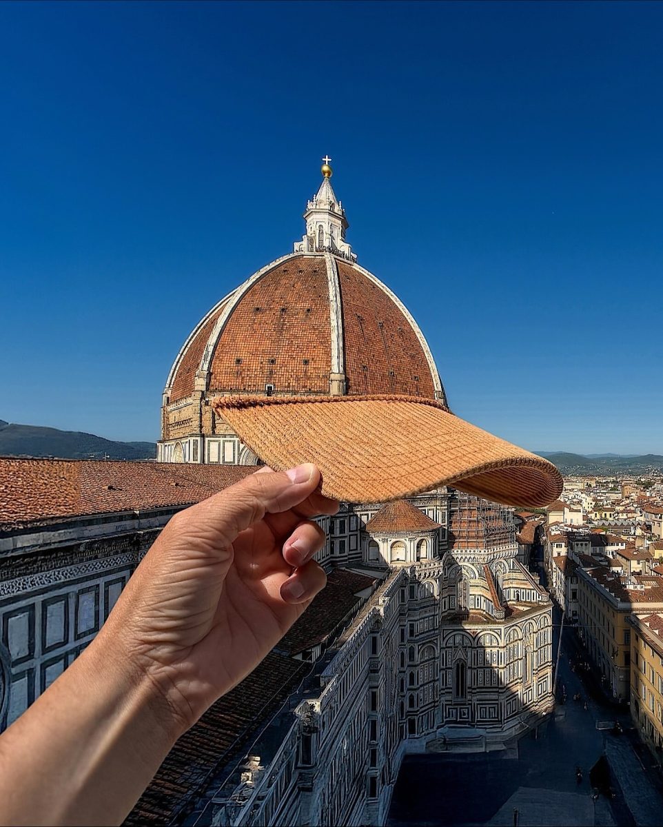 Ruka drží kšiltovku pred dómom vo Florencii za jasného slnečného dňa, modrá obloha v pozadí.