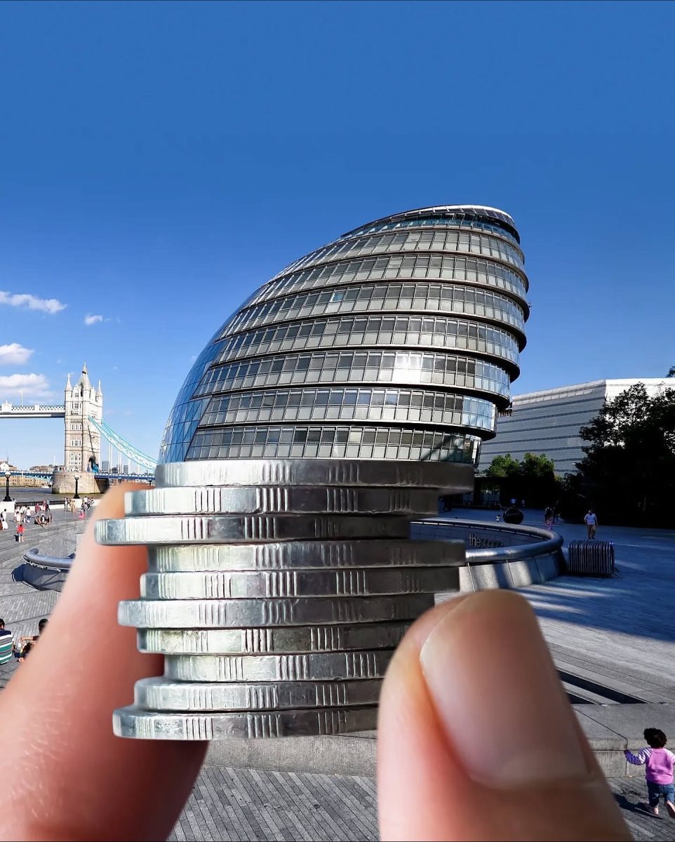 Osoba drží mince pred London City Hall, architektúra a perspektíva vytvárajú ilúziu nasadeného klobúka.