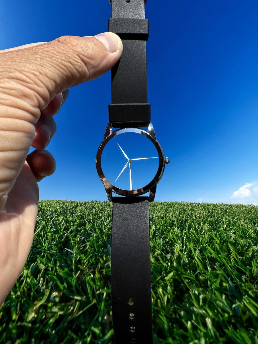 Náramkové hodinky držiace veternú turbínu na modrej oblohe a zelenej tráve, kreatívna perspektíva.