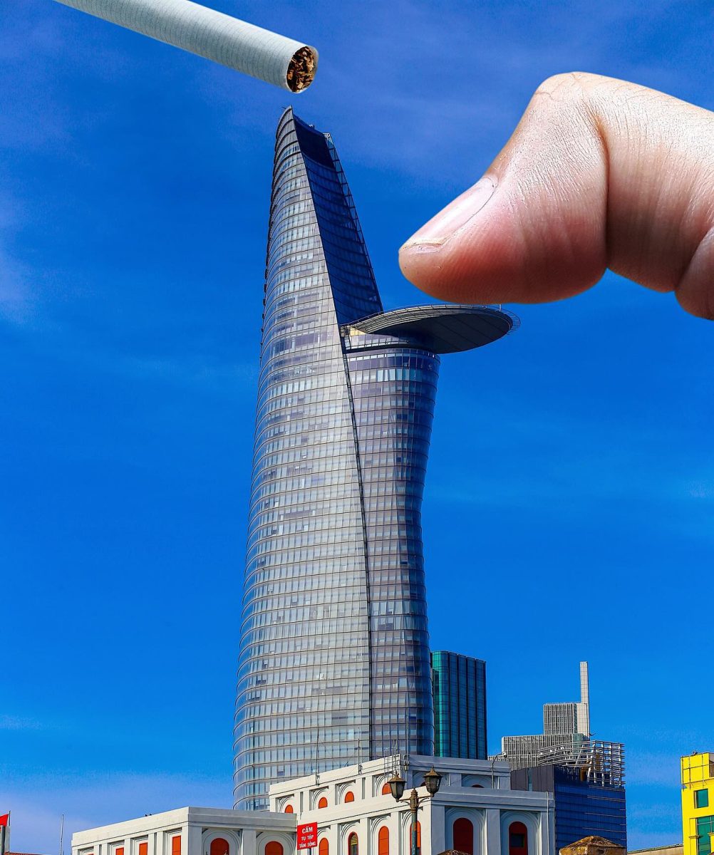Prst drží obrovskú cigaretu pri špičke modernej sklenenej budovy na modrej oblohe.