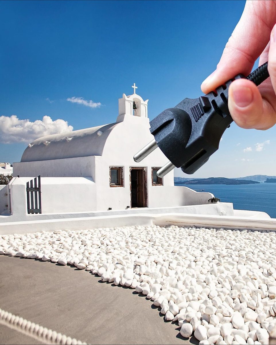 Nie je jasné, kto je na obrázku. Biely kostol na Santorini, ruka držiaca zástrčku pred modrou oblohou a Egejským morom.