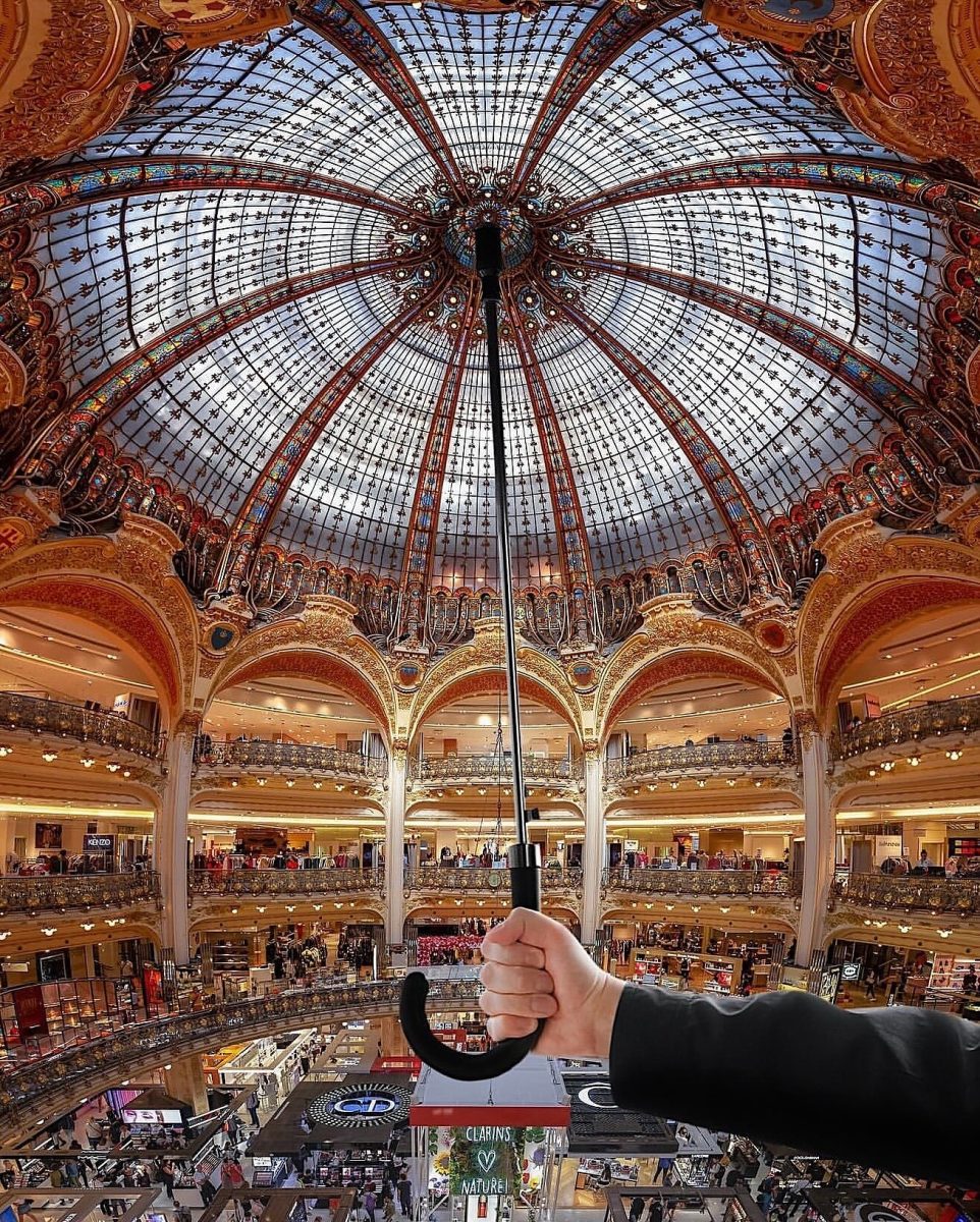 Ruka držiaca dáždnik pod veľkolepou vitrážovou kupolou luxusného obchodného domu plného ľudí.