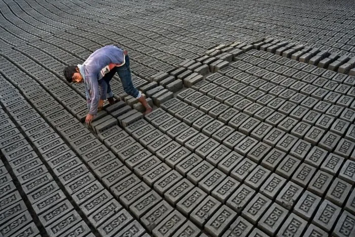 Muž pracujúci medzi stovkami tehál usporiadanými na sušenie v tehelní, pohľad na symetrické línie.