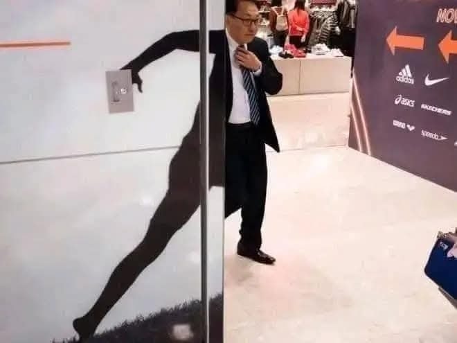 Muž kráča okolo steny s potlačou bežca, jeho telo vytvára ilúziu pokračovania siluety.