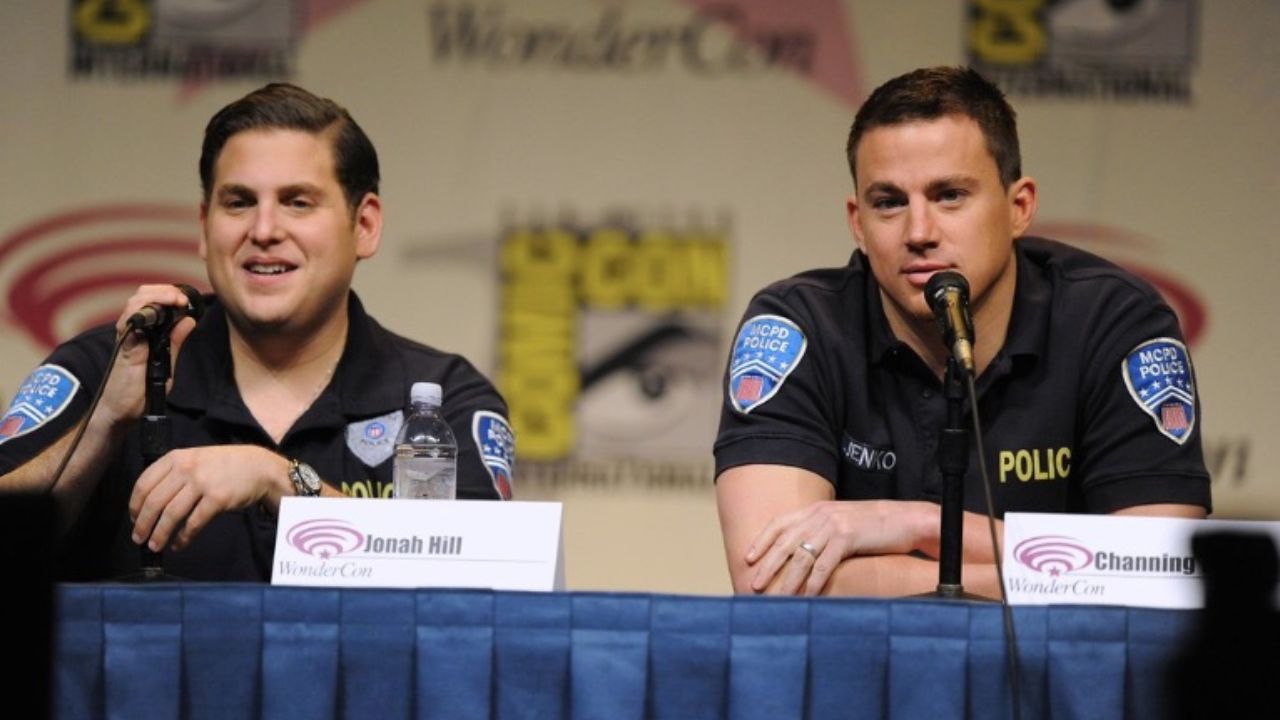 Dvojica mužov v policajných uniformách na panelovej diskusii s mikrofónmi na konferenčnom pódiu.