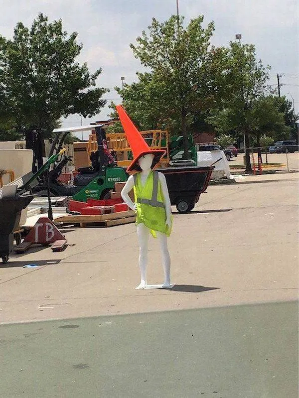 Manekýn na stavbe v reflexnej veste s obrovským kužeľom na hlave. Kreatívna pouličná dekorácia.