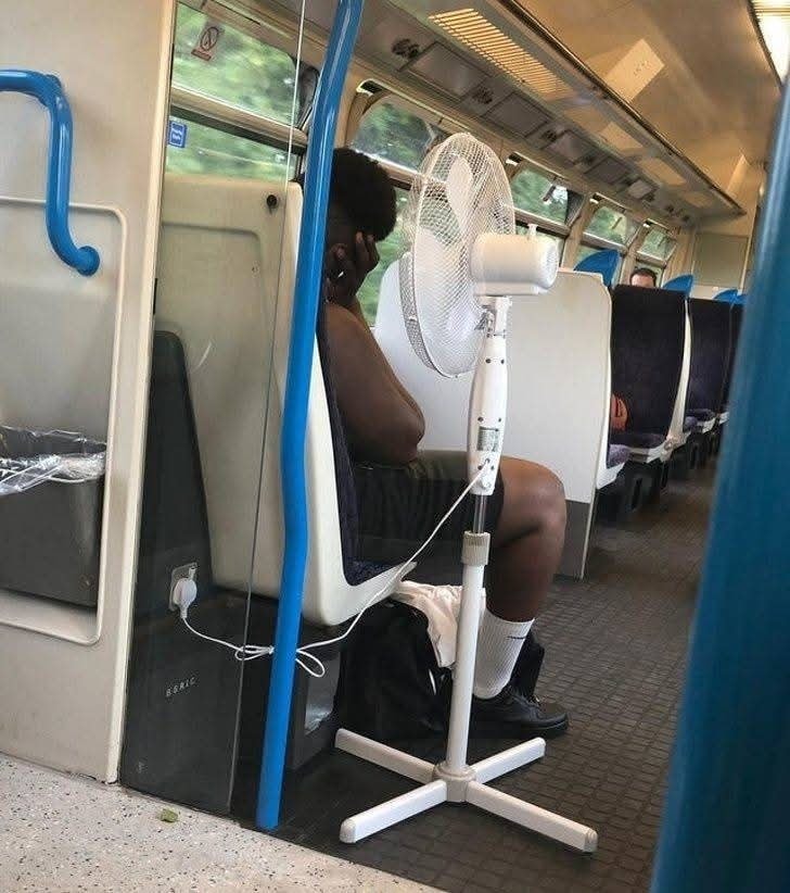 Osoba v vlaku s ventilátorom na ochladenie počas jazdy. Kreatívny spôsob zvládania horúčavy vo verejnej doprave.