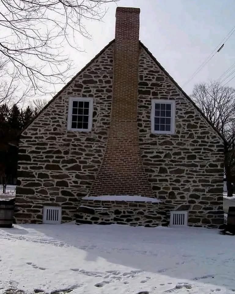 Kamenný dom s unikátnym, zakriveným komínom, zasnežený dvor, zimná krajina.