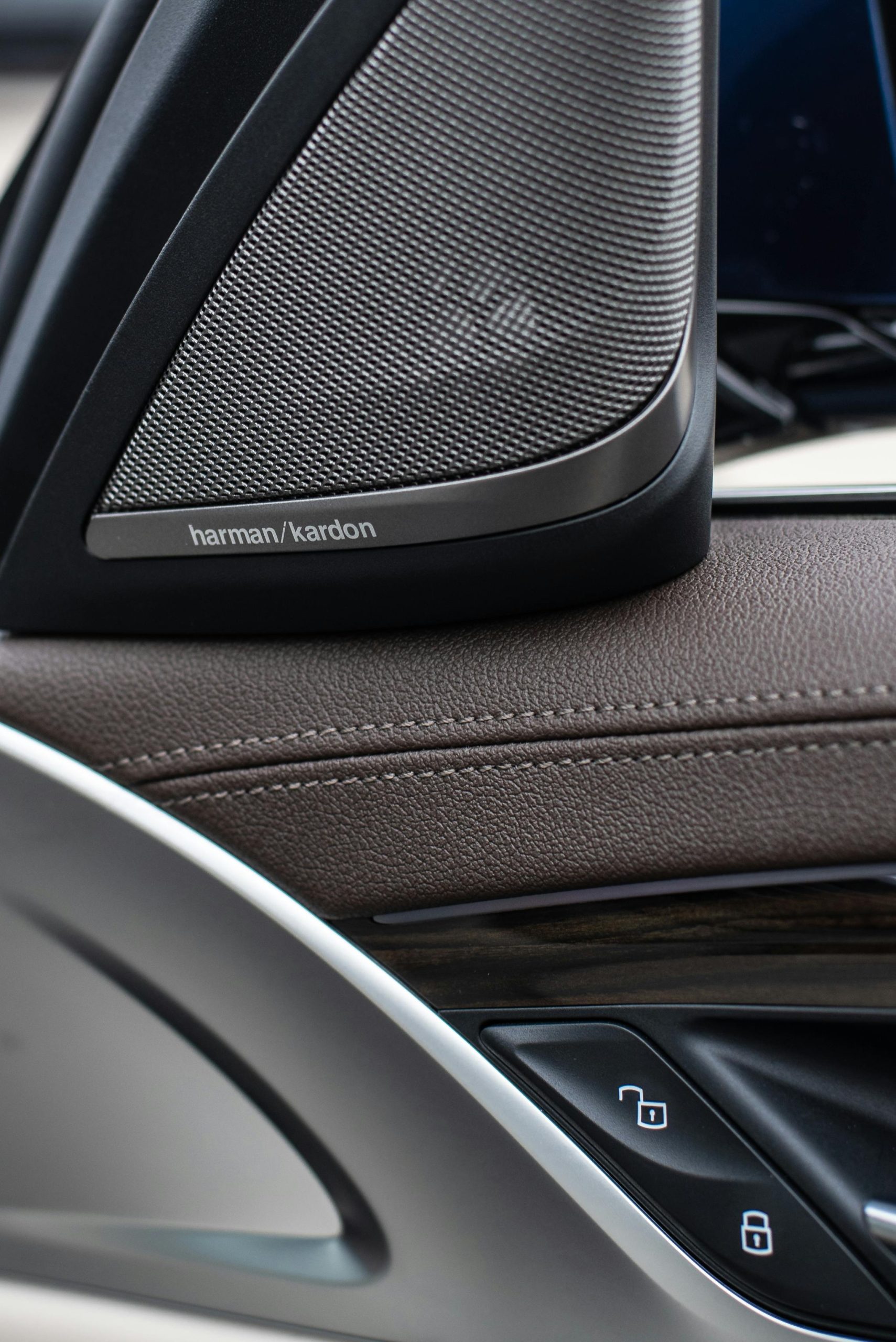 Detail reproduktora v interiéri auta s logom harman/kardon a ovládacími prvkami na dverách.