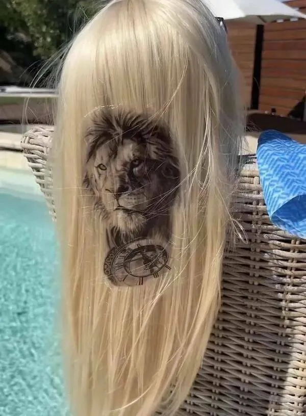 Dlhé blond vlasy s detailným tetovaním leva a hodiniek pri bazéne.