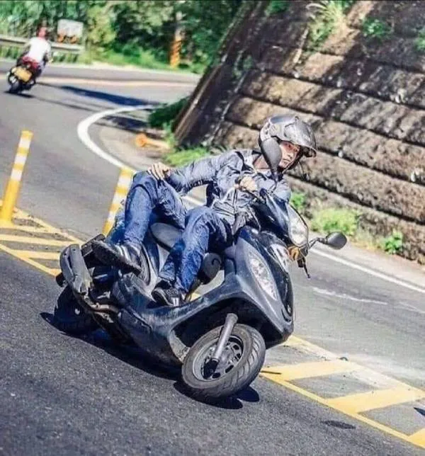 Osoba na skútri sa nakláňa pri zákrute na ceste, zvyšuje tak stabilitu a bezpečnosť jazdy.