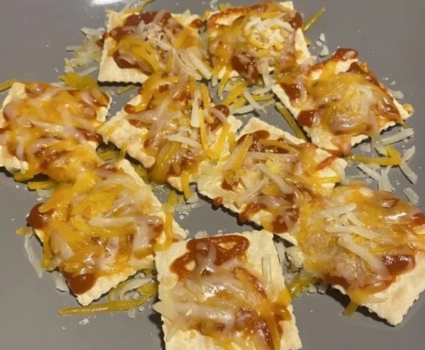 Krekry s roztaveným syrom a omáčkou podávané na šedom tanieri, ideálne ako rýchle občerstvenie.