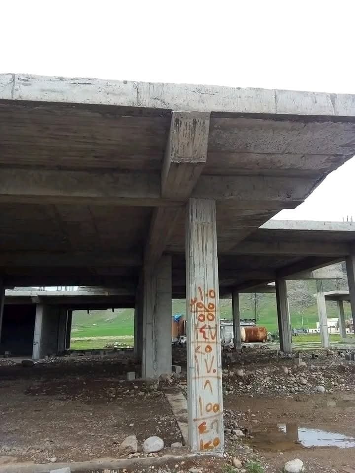 Nedokončená železobetónová stavba so stĺpmi a povrchom s graffiti, v pozadí zelená krajina.