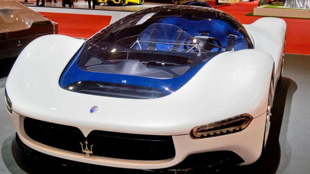 Futuristický biely superšportový automobil s modrým interiérom na výstave, vystavený na červenom koberci.