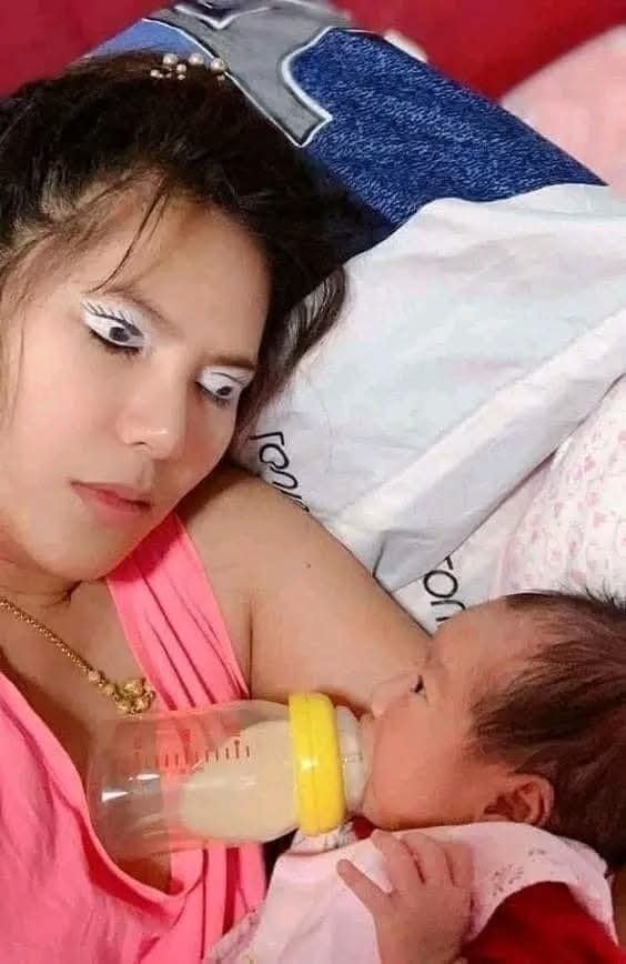 Matka s výrazným líčením a dieťa, ktoré pije mlieko z fľaše, ležia spolu na posteli.