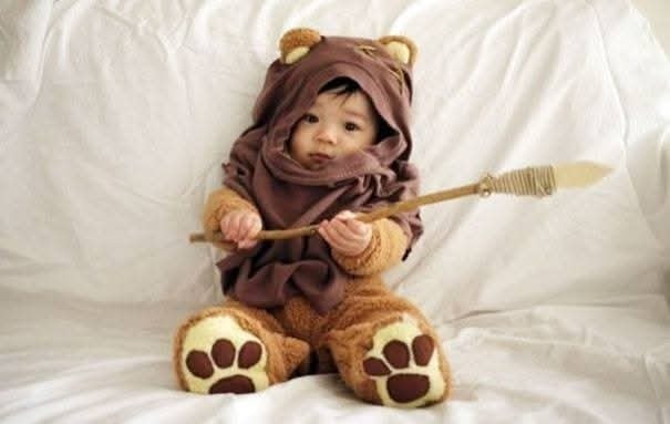 Dieťa v kostýme Ewoka sedí na pohovke a drží kopiju, rozkošná sci-fi inšpirácia na Halloween.