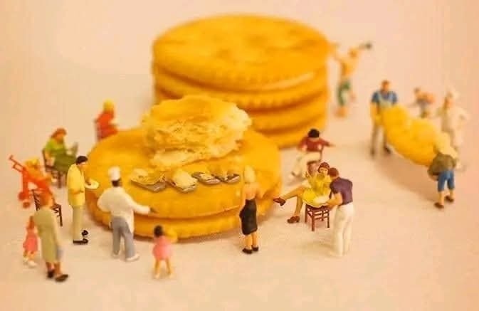 Miniatúrne postavičky sedia a pracujú okolo obrovských sušienok na jemnom pozadí. Kreatívna scéna z každodenného života.