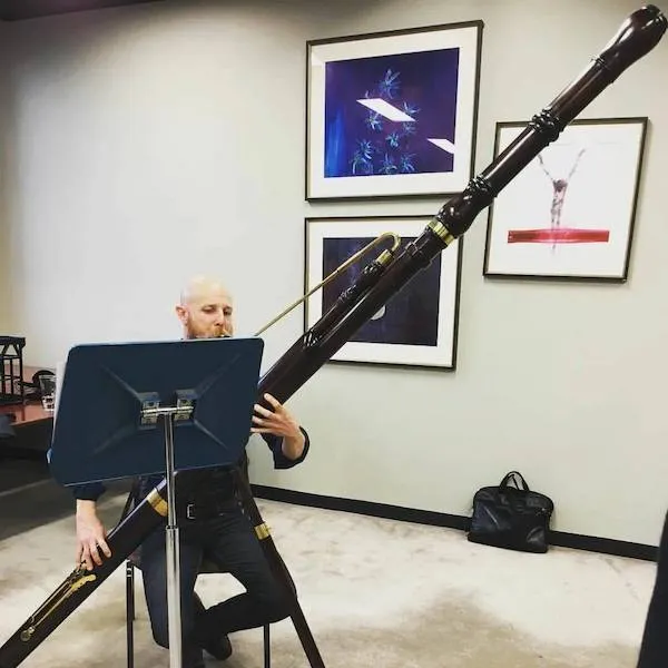 Muž hrá na obrovskom dychovom nástroji pri stojane s notami v umeleckej miestnosti.