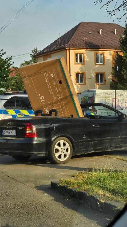 Auto s veľkým televízorom v zadnej časti vedľa policajného auta na ulici.