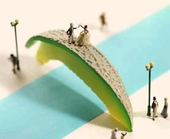 Miniatúrny nevesta a ženích na moste z melónovej kôry, dekoratívne lampy, modro-biely pruhovaný povrch.
