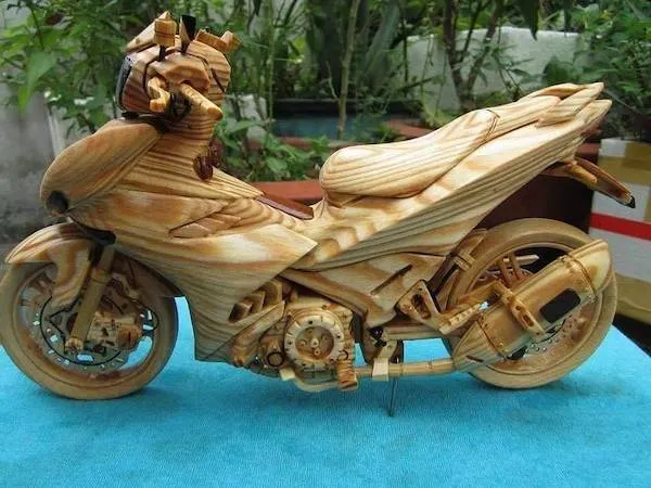 Drevený model motorky umiestnený na modrej látke s detailným spracovaním a prirodzeným dreveným vzorom.