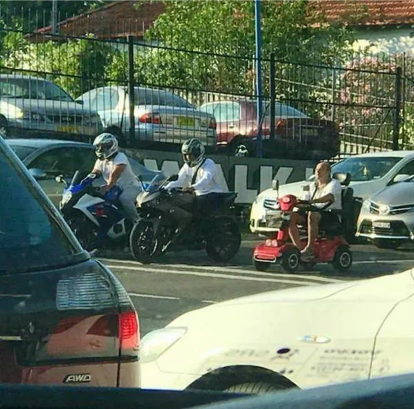 Motorkári a muž na elektrickom vozíku stojaci na parkovisku medzi autami.