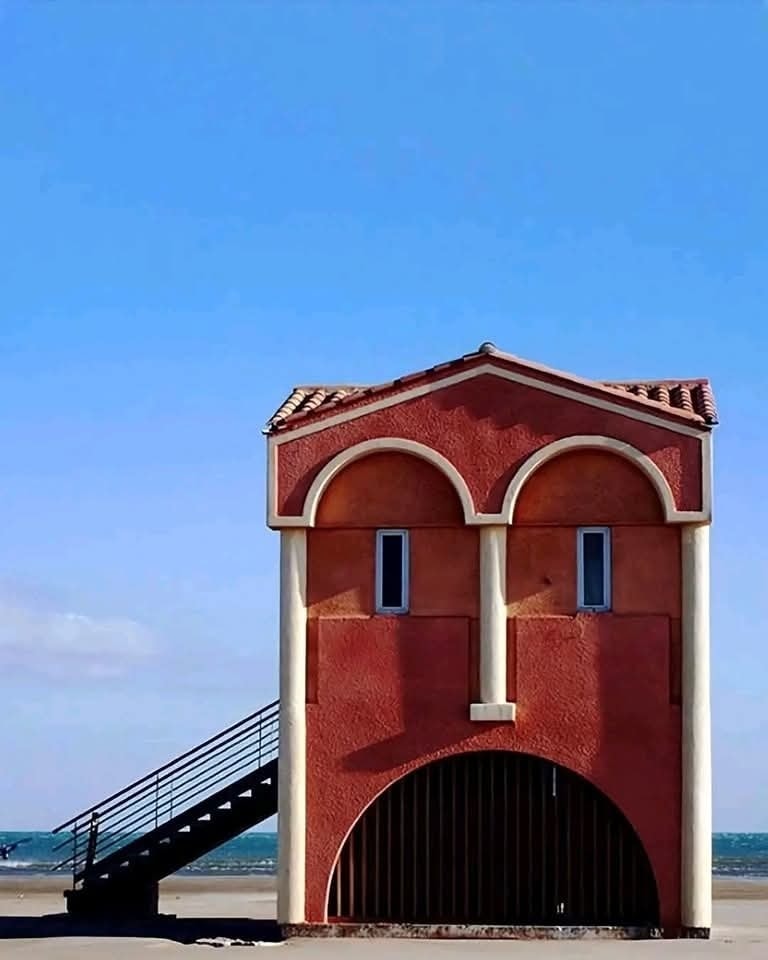 Červená budova na pláži vyzerá ako tvár s modrou oblohou v pozadí.