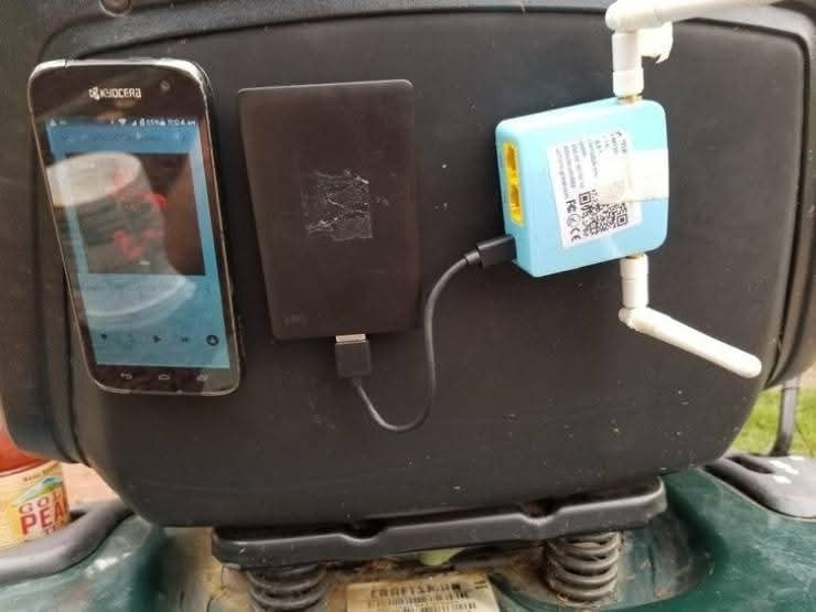 Mobil, externý disk a smerovač zapojené v provizórnom nastavení na improvizovanej podložke.