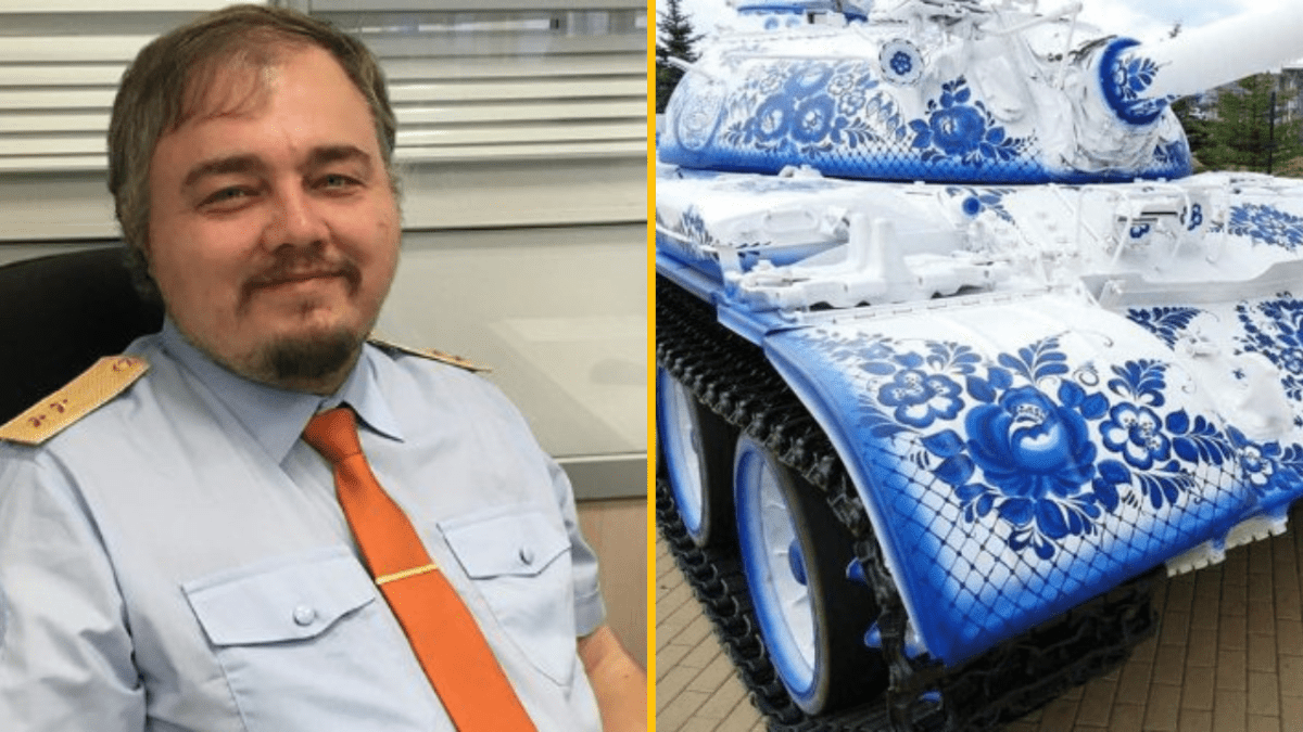 Muž v uniforme s oranžovou kravatou, vedľa tanku s modro-bielym folklórnym vzorom.