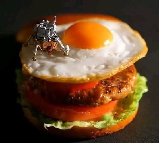 Miniatúrny lunárny modul pristáva na hamburgeri s volským okom, šalátom a paradajkou. Kreatívna kompozícia jedla.