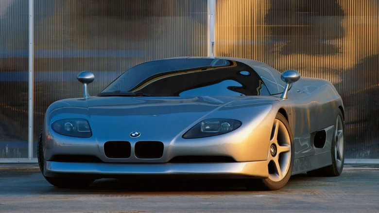 Strieborný športový koncept BMW s moderným dizajnom pred sklenenou stenou v západe slnka.