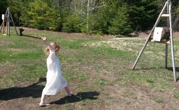 Dieťa v bielych šatách hádže sekeru na cieľ vonku na tráve.