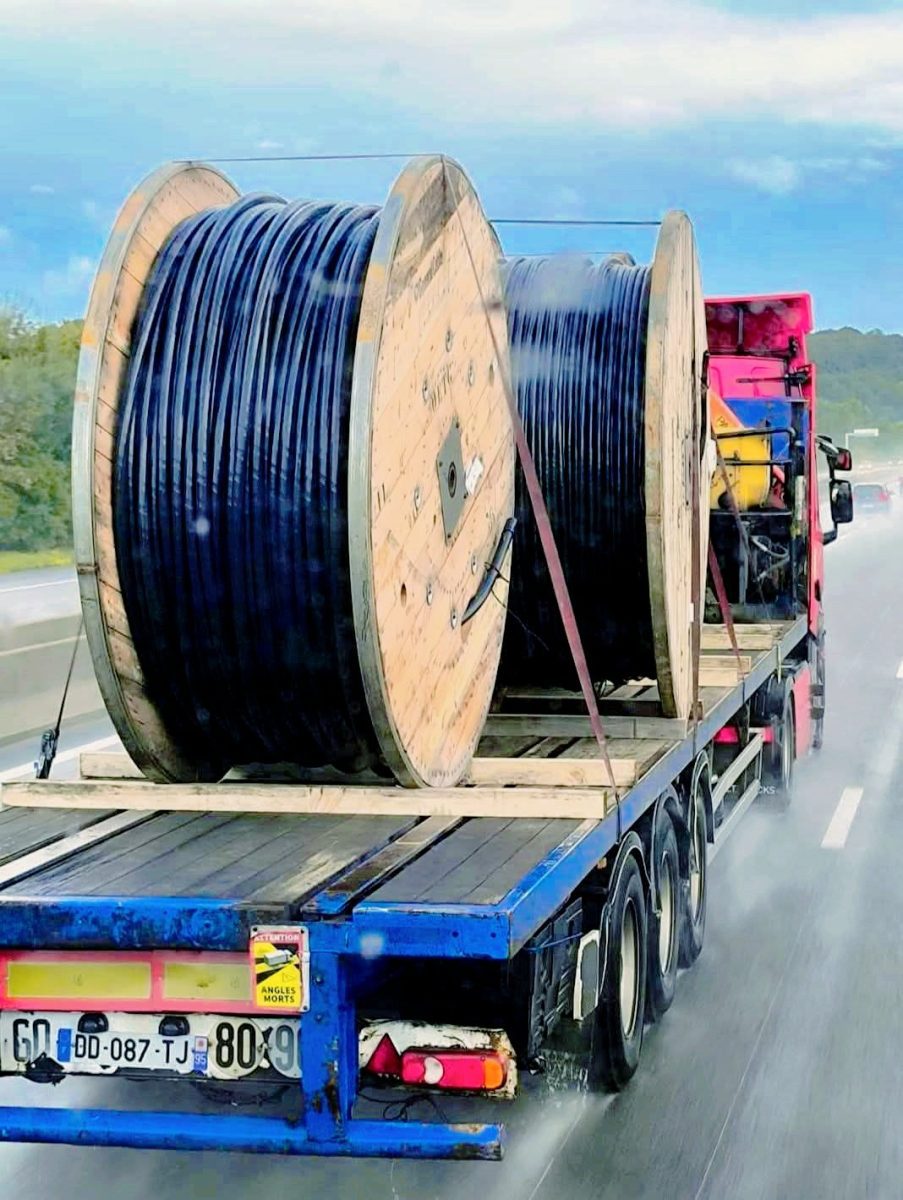 Kamión preváža veľké cievky s káblami po diaľnici v daždi.