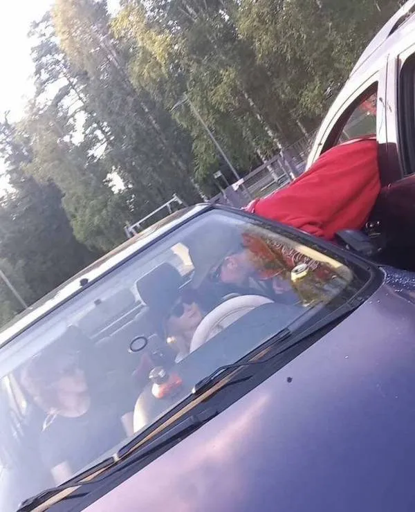 Ľudia sediaci v aute na parkovisku, okolitá príroda a svetlo prenikajúce cez stromy na pozadí.