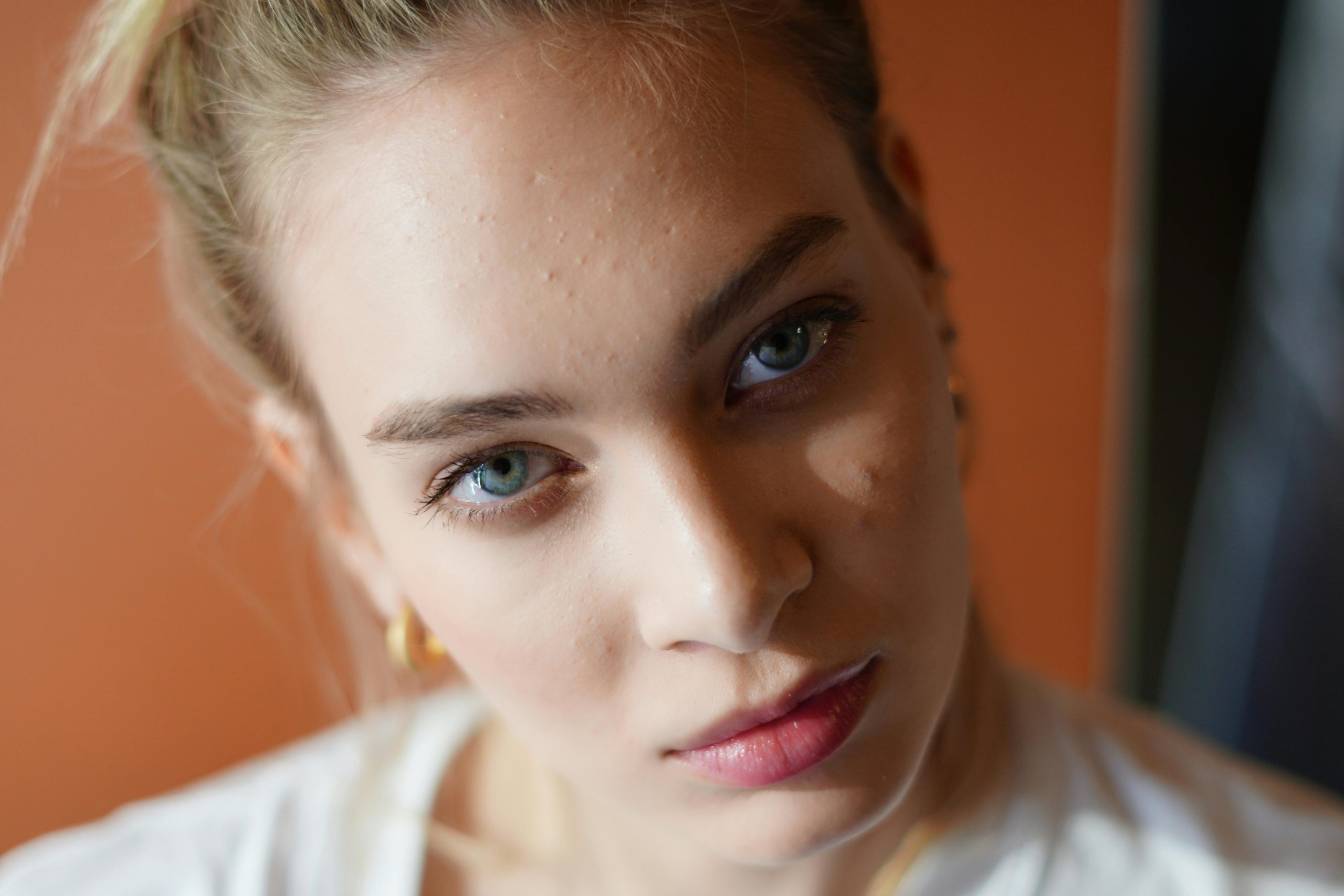 Portrét ženy s modrými očami a blede tvárou, ktorá sa pozerá priamo do objektívu.