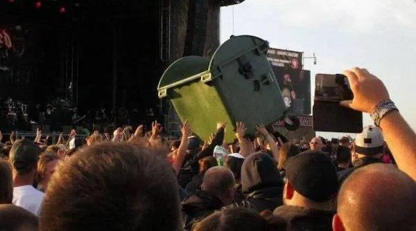 Koncert, dav fanúšikov zábavne prenáša zelený kontajner nad hlavami v uvoľnenej atmosfére.