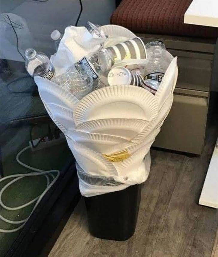 Koš s preplnenými jednorazovými taniermi a fľašami v kancelárii.