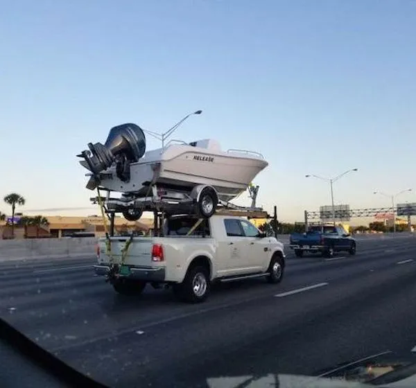 Pickup s loďou na streche jazdí po diaľnici za slnečného dňa, neobvyklá preprava vodného plavidla.