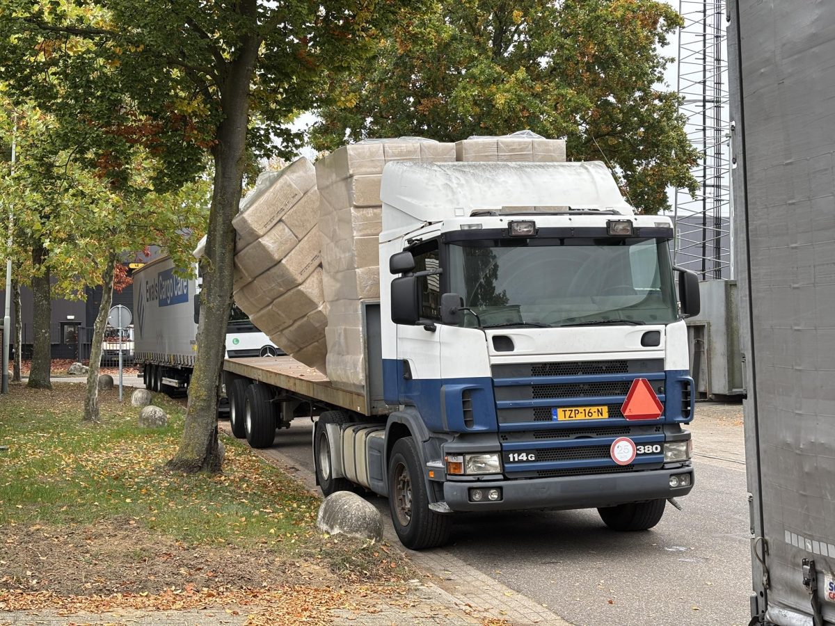 Nákladné auto prepravuje veľké balíky po ceste lemovanej stromami na jeseň.