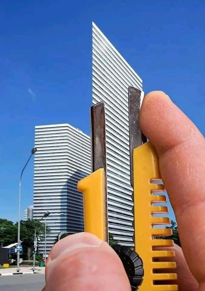 Ruka drží nôž, ktorý vizuálne prerezáva budovu v pozadí na modrom pozadí. Optická ilúzia rezu.