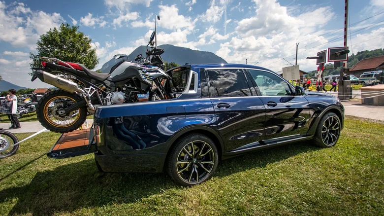 Modré auto s naloženou motorkou na lúke, v pozadí hory a modrá obloha s bielymi oblakmi.