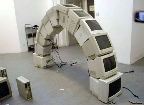 Oblúk zložený z CRT monitorov, kreatívna inštalácia v industriálnom priestore s počítačovými komponentmi.