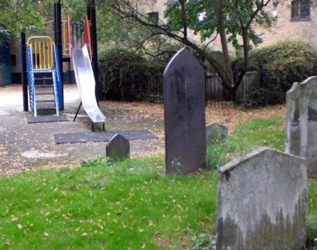 Detské ihrisko vedľa starého cintorína s náhrobnými kameňmi, kontrast medzi zábavou a históriou.