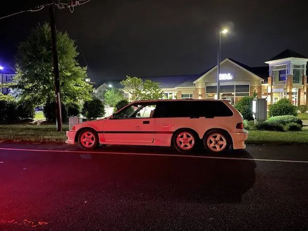 Klasické auto v noci zaparkované pri osvetlenej budove, jemne osvetlené mestskými svetlami.