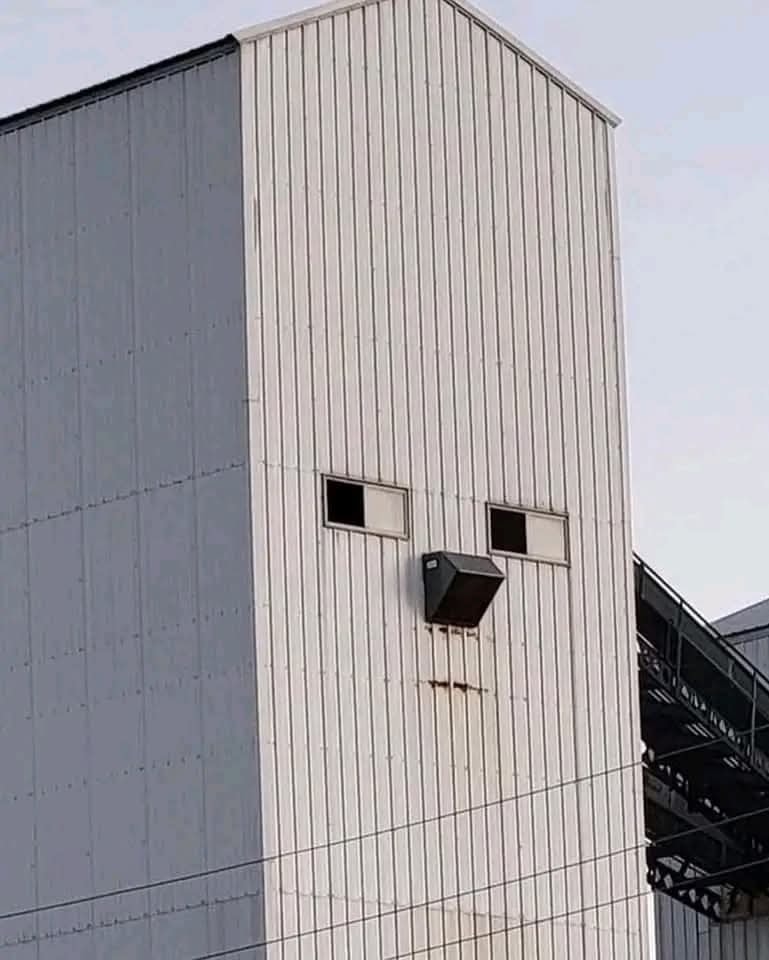 Budova s oknami pripomínajúcimi tvár na priemyselnom pozadí, podobná s výzorom človeka.